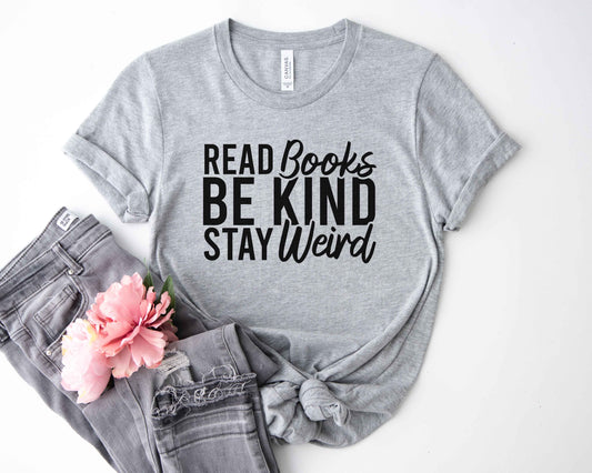 An althetic heather color shirt with the saying "Read books be kind stay weird"