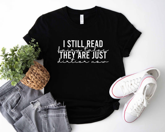 A black color shirt with the saying "i still read fairy tales they are just dirtier now"