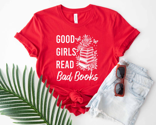 Red t-shirt with 'Good Girls Read Bad Books' text and floral design, paired with sunglasses and denim shorts on a white background.