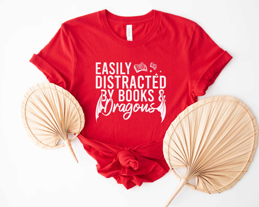 A red color shirt with the saying "Easily distracted by books and dragons"