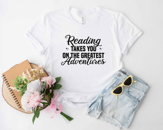 A white color shirt with the saying "Reading takes you on the greatest adventures"