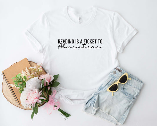 A white color shirt with the saying "Reading is a ticket to adventure"