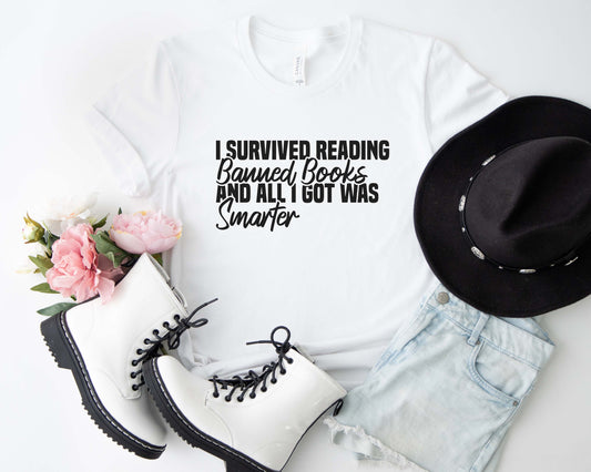 A white color shirt with the saying "I Survived Reading Banned Books And All I Got Was Smarter"