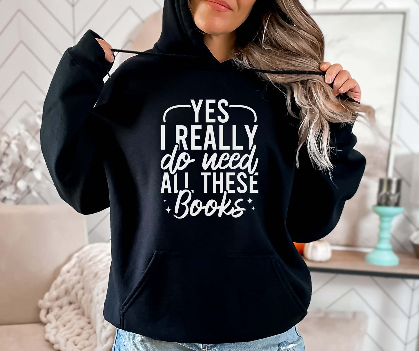 Person wearing a black hoodie with text 'Yes I really do need all these books' in a home setting.