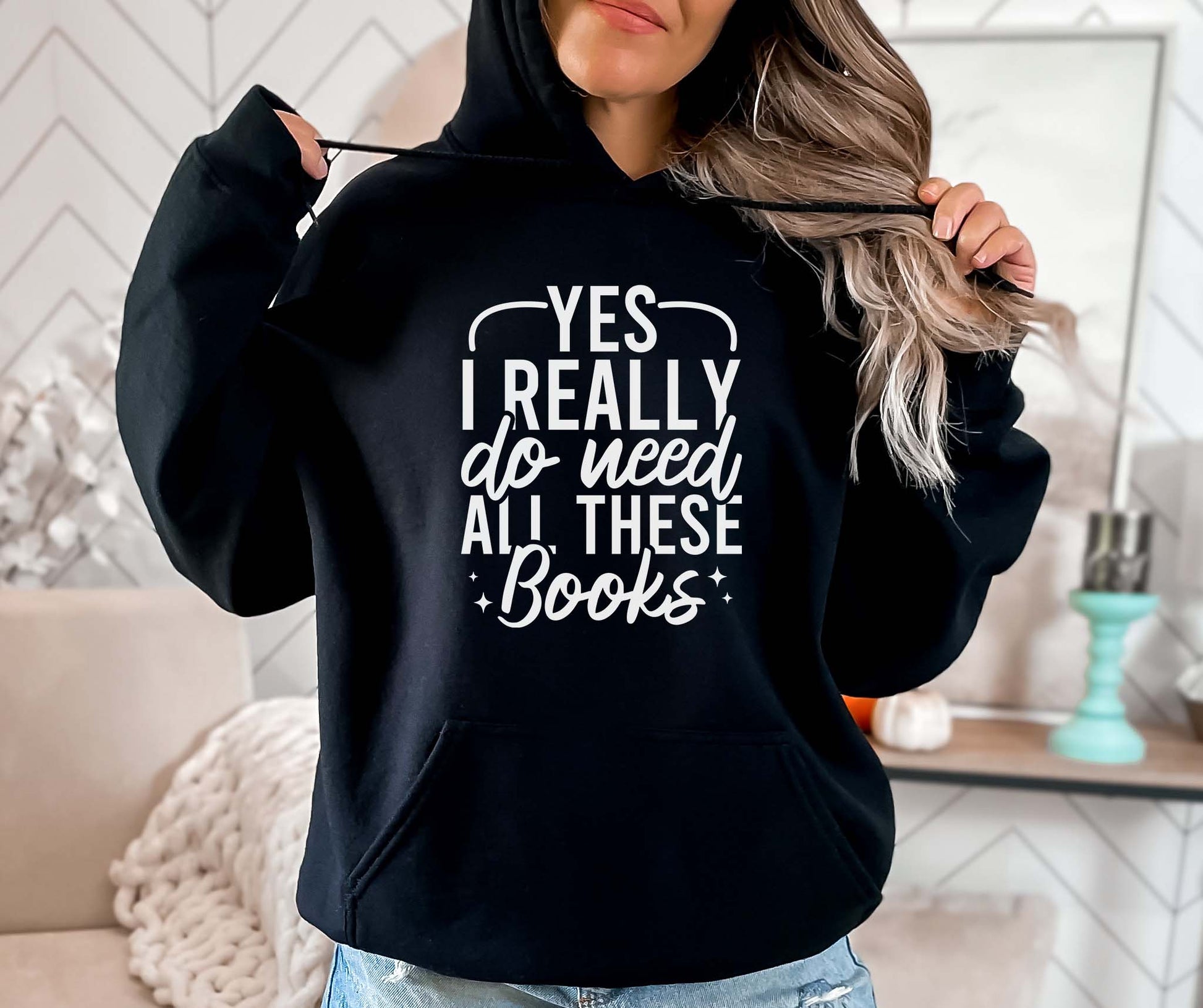 Person wearing a black hoodie with text 'Yes I really do need all these books' in a home setting.