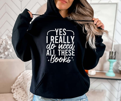 Person wearing a black hoodie with text 'Yes I really do need all these books' in a home setting.