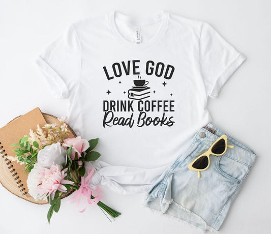 White t-shirt with 'Love God, Drink Coffee, Read Books' text on a white background with accessories.