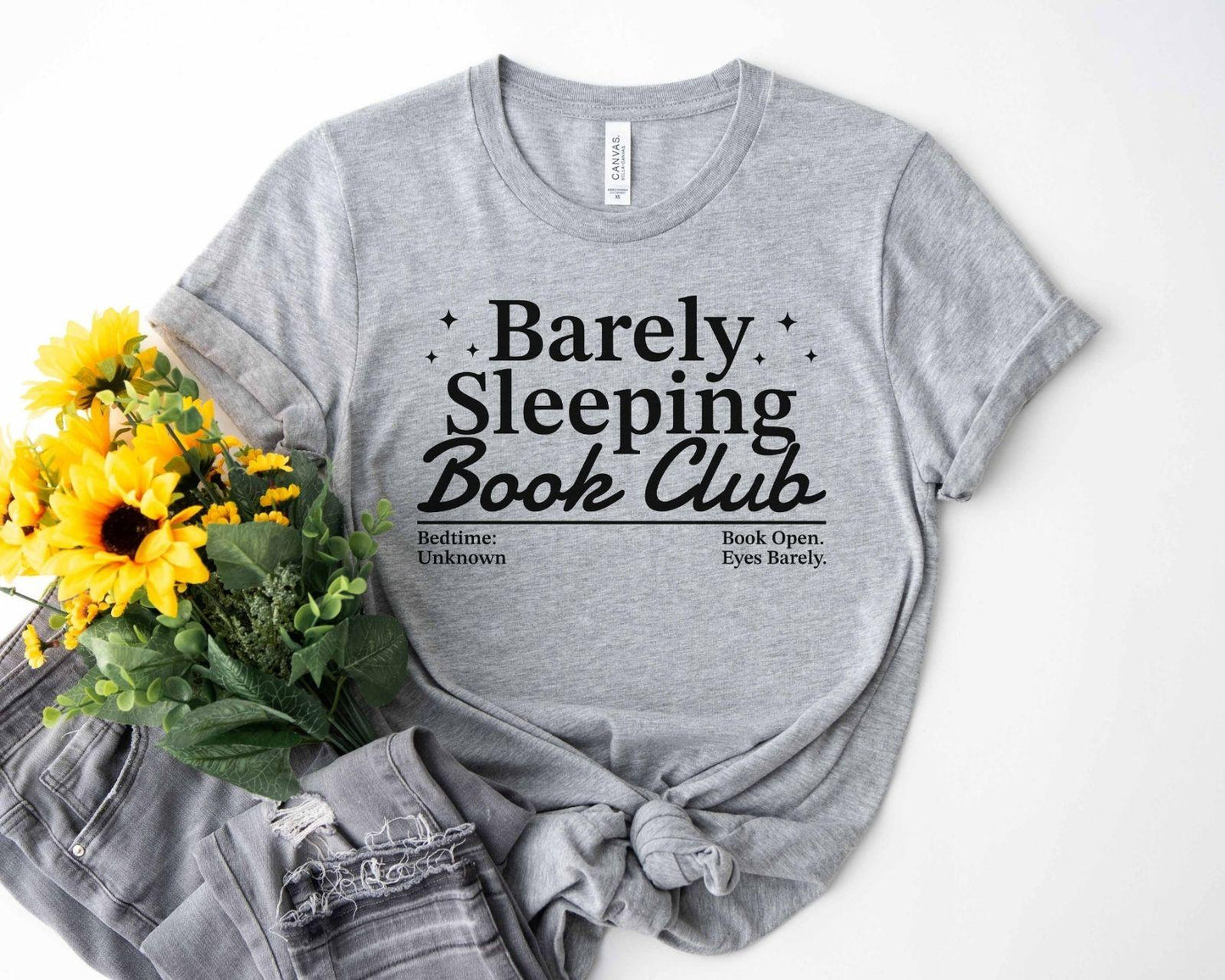 A bella canvas 3001 shirt with the saying "Barely sleeping book club"