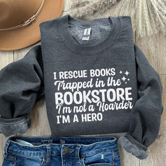 A dark heather color sweatshirt with the saying "I rescue books trapped in the bookstore im not a hoarder im a hero"