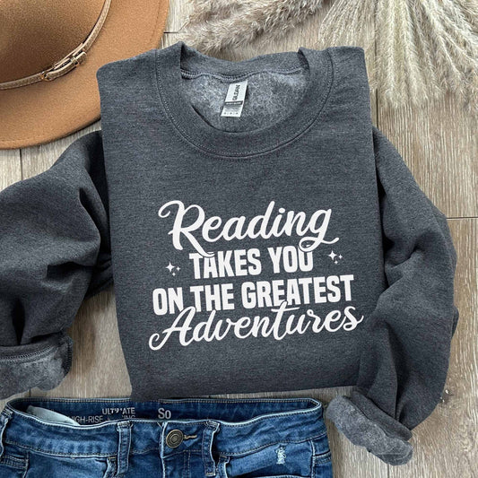 A dark heather color sweatshirt with the saying "Reading takes you on the greatest adventures"