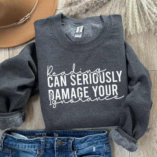 A dark heather color sweatshirt with the saying "Reading can seriously damage your ignorance"