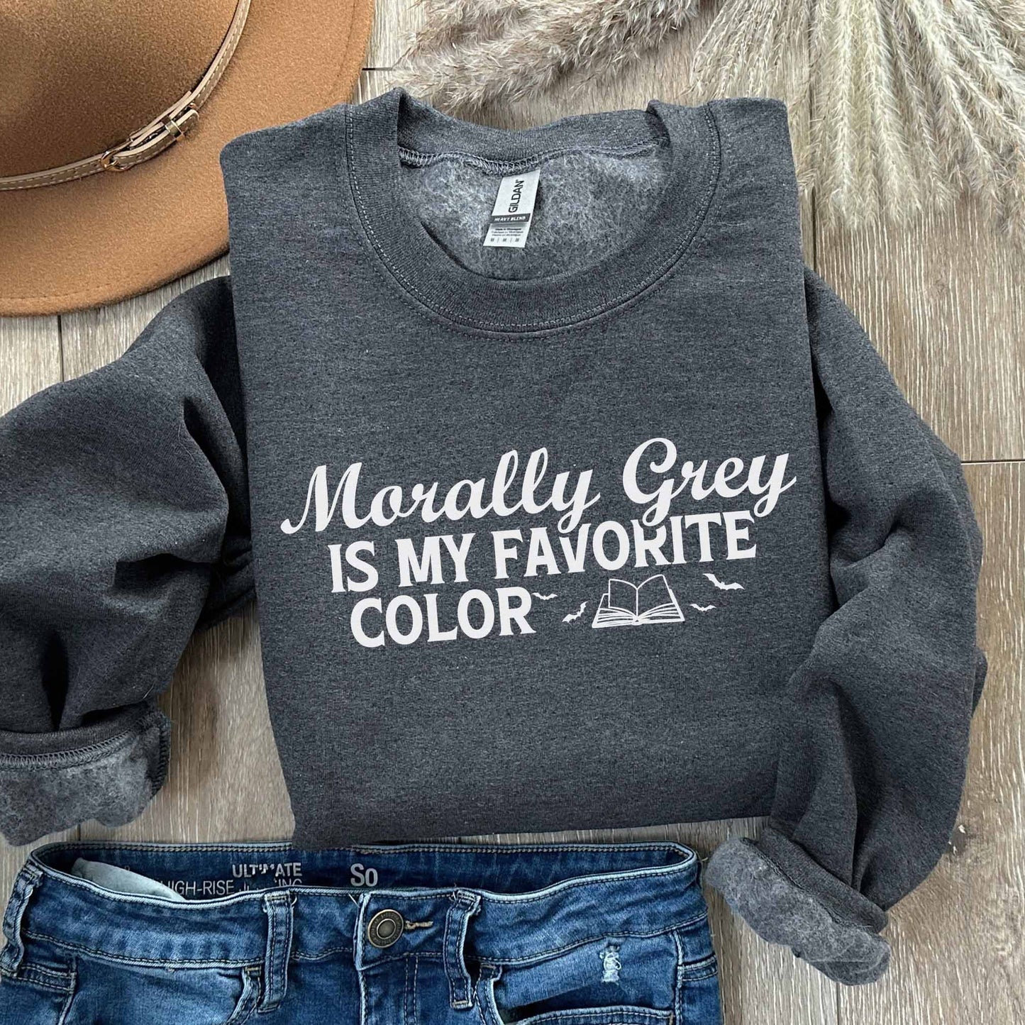 Dark heather sweatshirt with text 'Morally Grey is my favorite color' on a wooden surface with a hat and jeans.