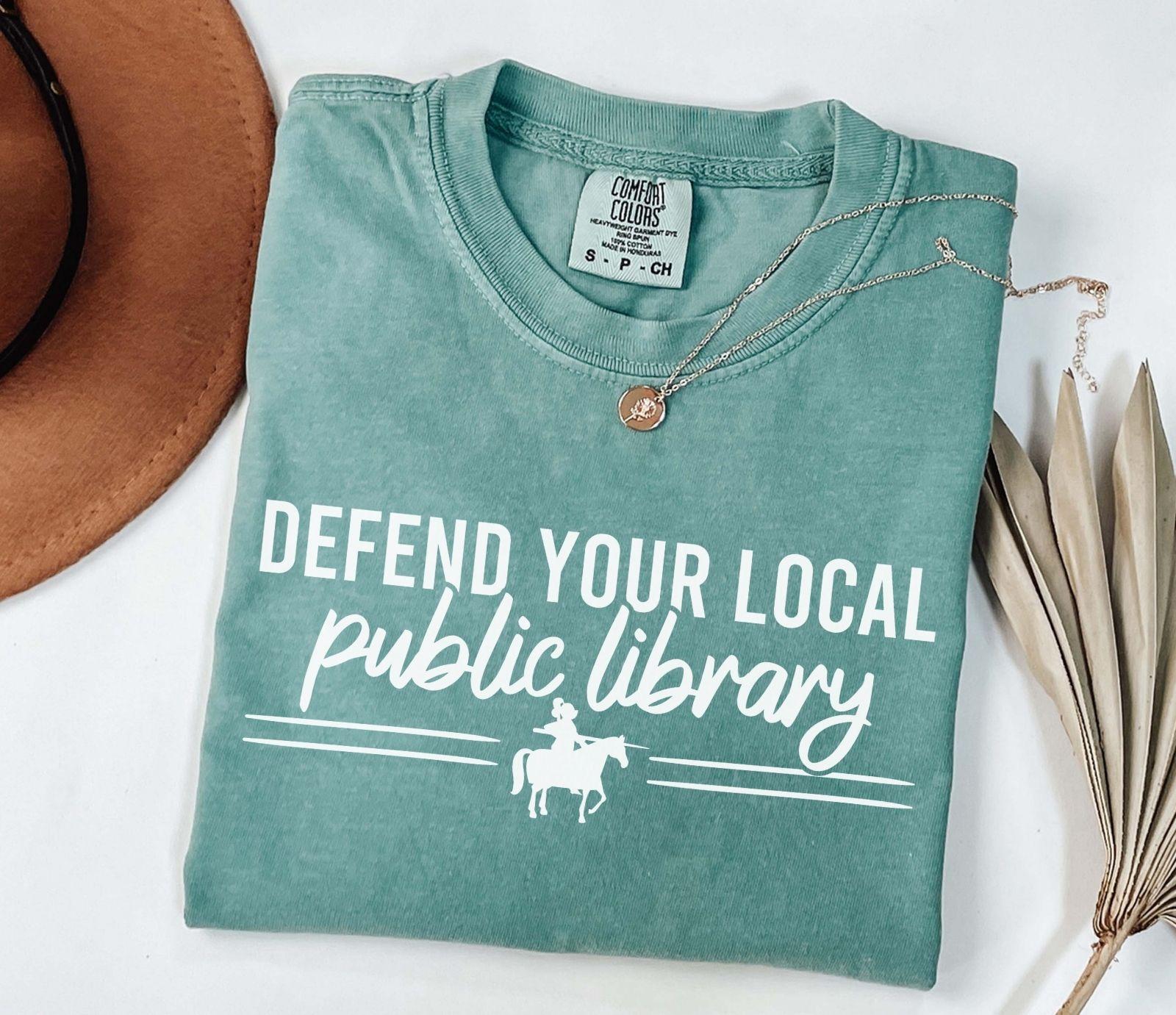 A comfort colors shirt with the saying "Defend your local public library"