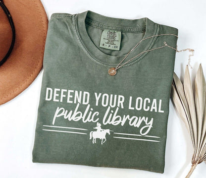 A comfort colors shirt with the saying "Defend your local public library"