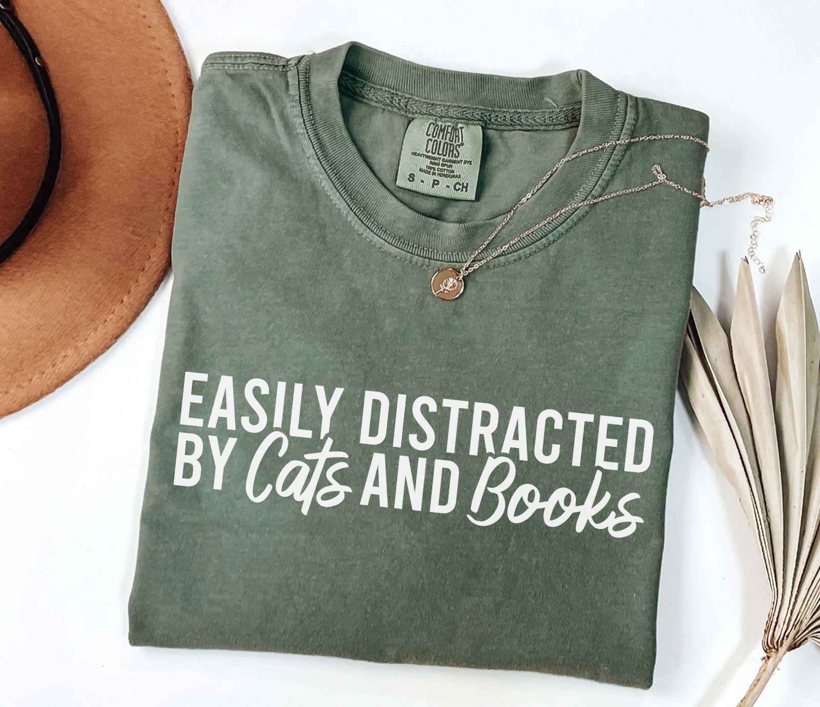 A comfort colors® shirt with the saying "Easily distracted by cats and books"