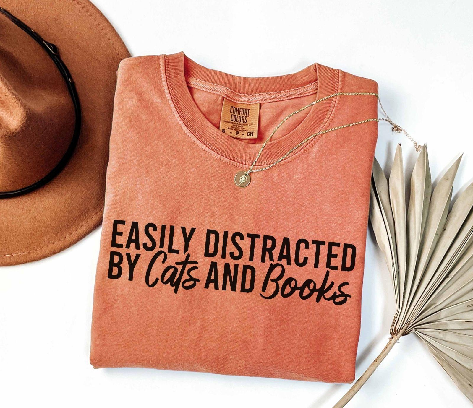 A comfort colors® shirt with the saying "Easily distracted by cats and books"