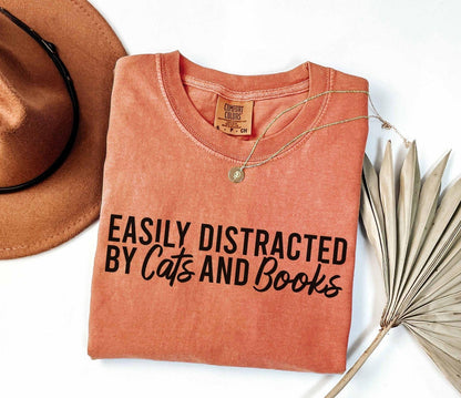A comfort colors® shirt with the saying "Easily distracted by cats and books"