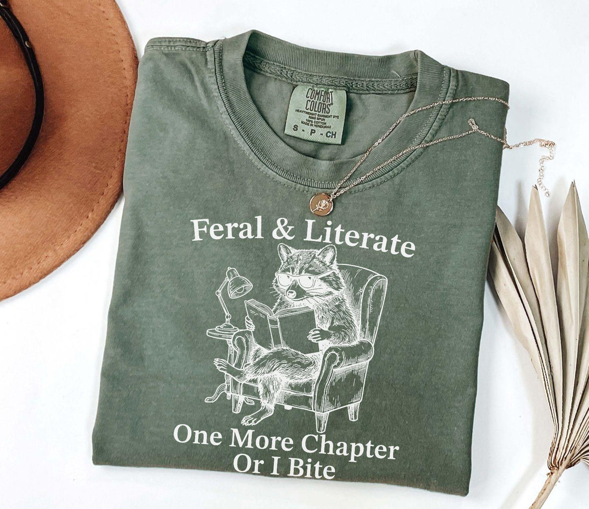 A comfort colors® shirt with the saying "Feral And Literate One More Chapter Or I Bite"