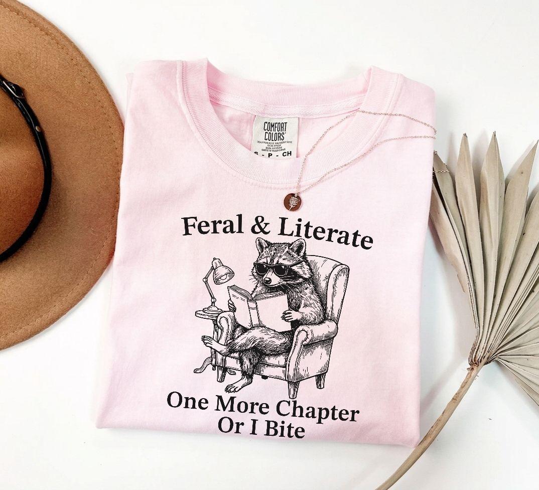 A comfort colors® shirt with the saying "Feral And Literate One More Chapter Or I Bite"