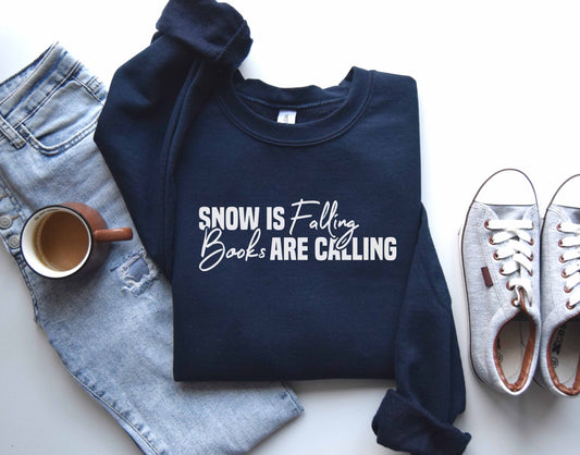 A navy color sweatshirt with the saying "Snow is falling books are calling"