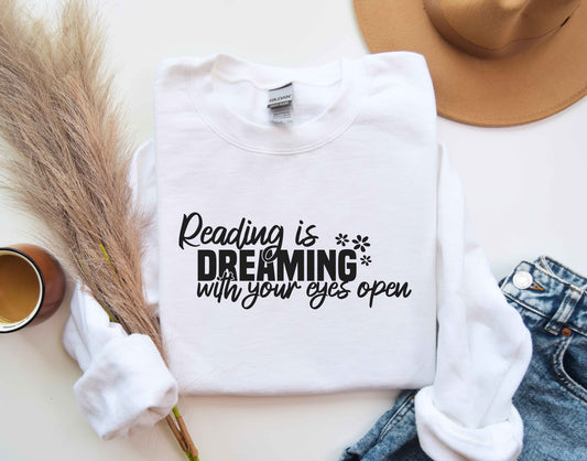 A white color sweatshirt with the saying "Reading is dreaming with your eyes open"