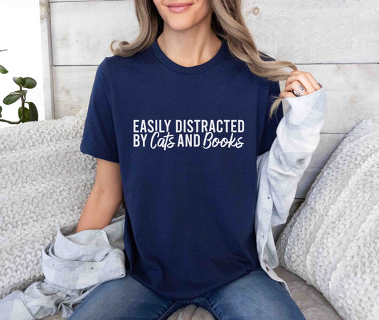 A navy color shirt with the saying "Easily distracted by cats and books"