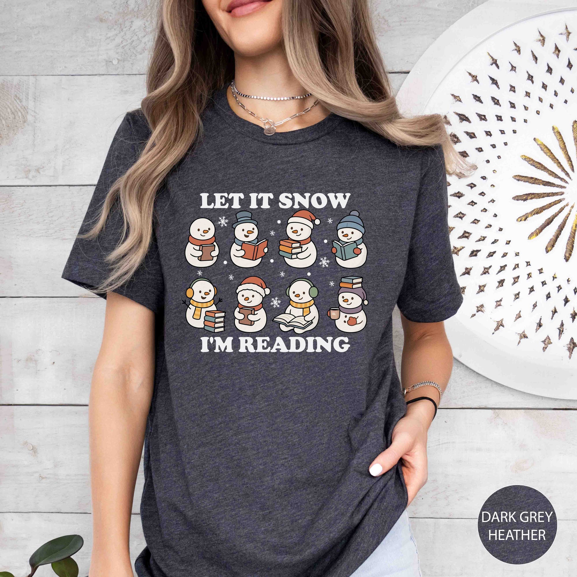 Person wearing a dark grey heather t-shirt with snowman graphics and text, standing against a light wooden wall.