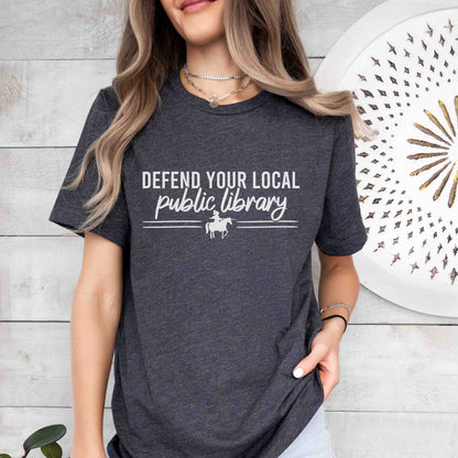 Person wearing a dark gray heather t-shirt with 'Defend Your Local Public Library' text and graphic.