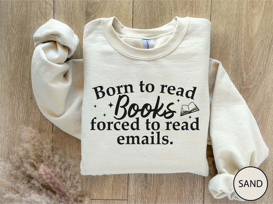 Folded sand color sweatshirt with text 'Born to read Books forced to read emails.' on a wooden surface.