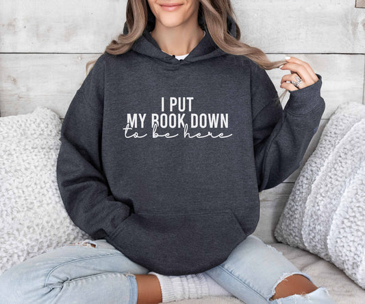 A dark heather color hoodie with the saying "I put my book down to be here"