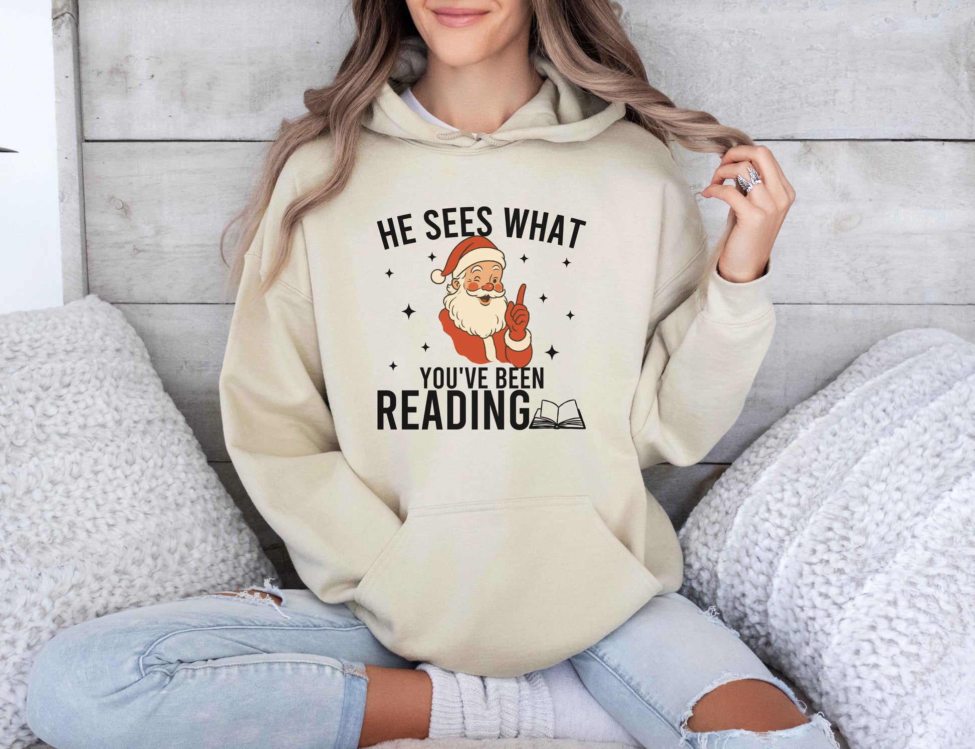 Person wearing a sand hoodie with a Santa Claus graphic and text, sitting on a couch.