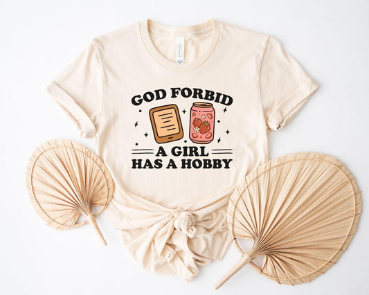A bella canvas 3001 shirt with the saying "god forbid a girl has a hobby"