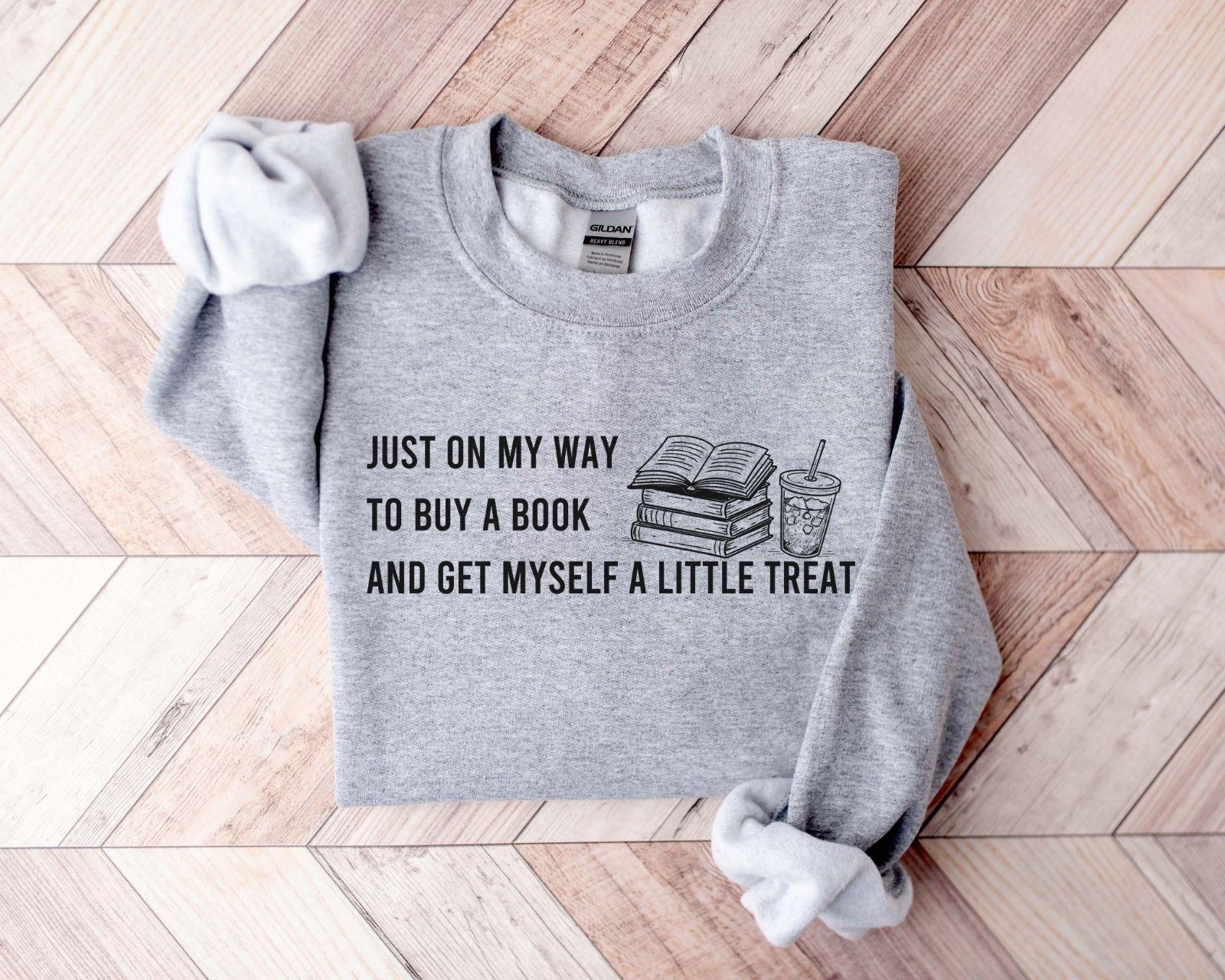 A dark heather color Gildan 18000 sweatshirt with the saying "Just on my way to buy a boook and get myself a little treat"