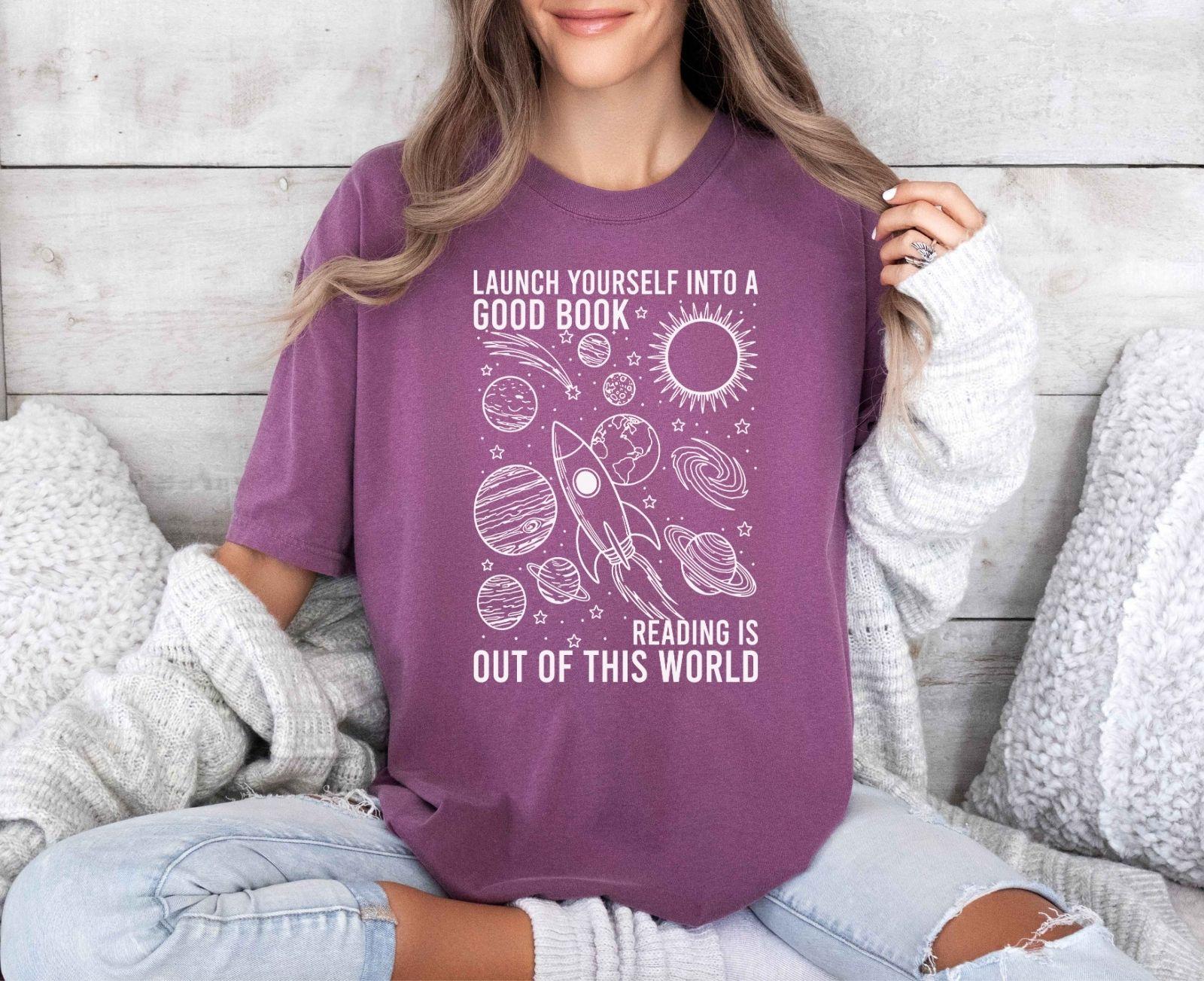 A comfort colors® shirt with the saying "launch yourself into a good book reading is out of this world"