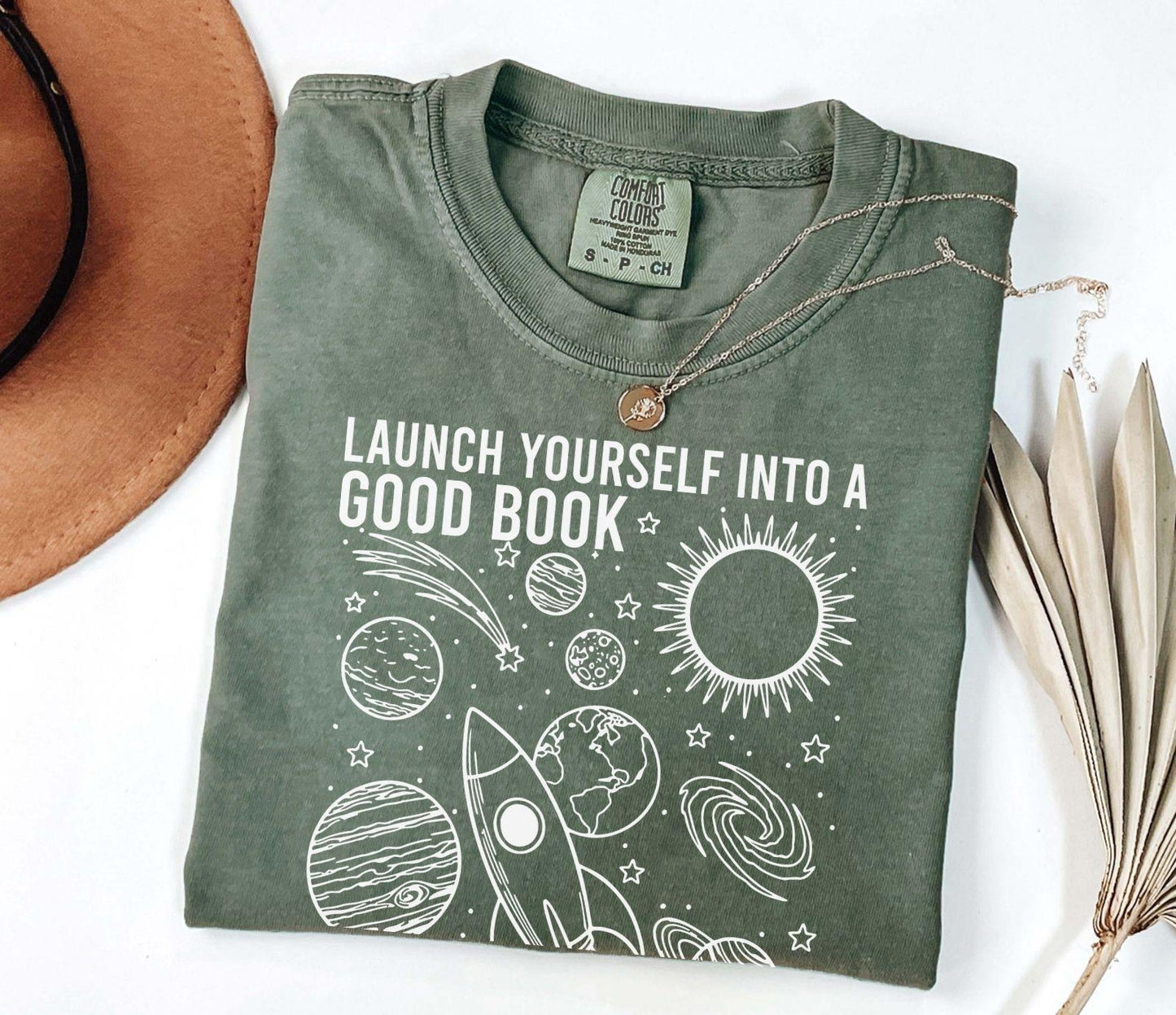 A comfort colors® shirt with the saying "launch yourself into a good book reading is out of this world"