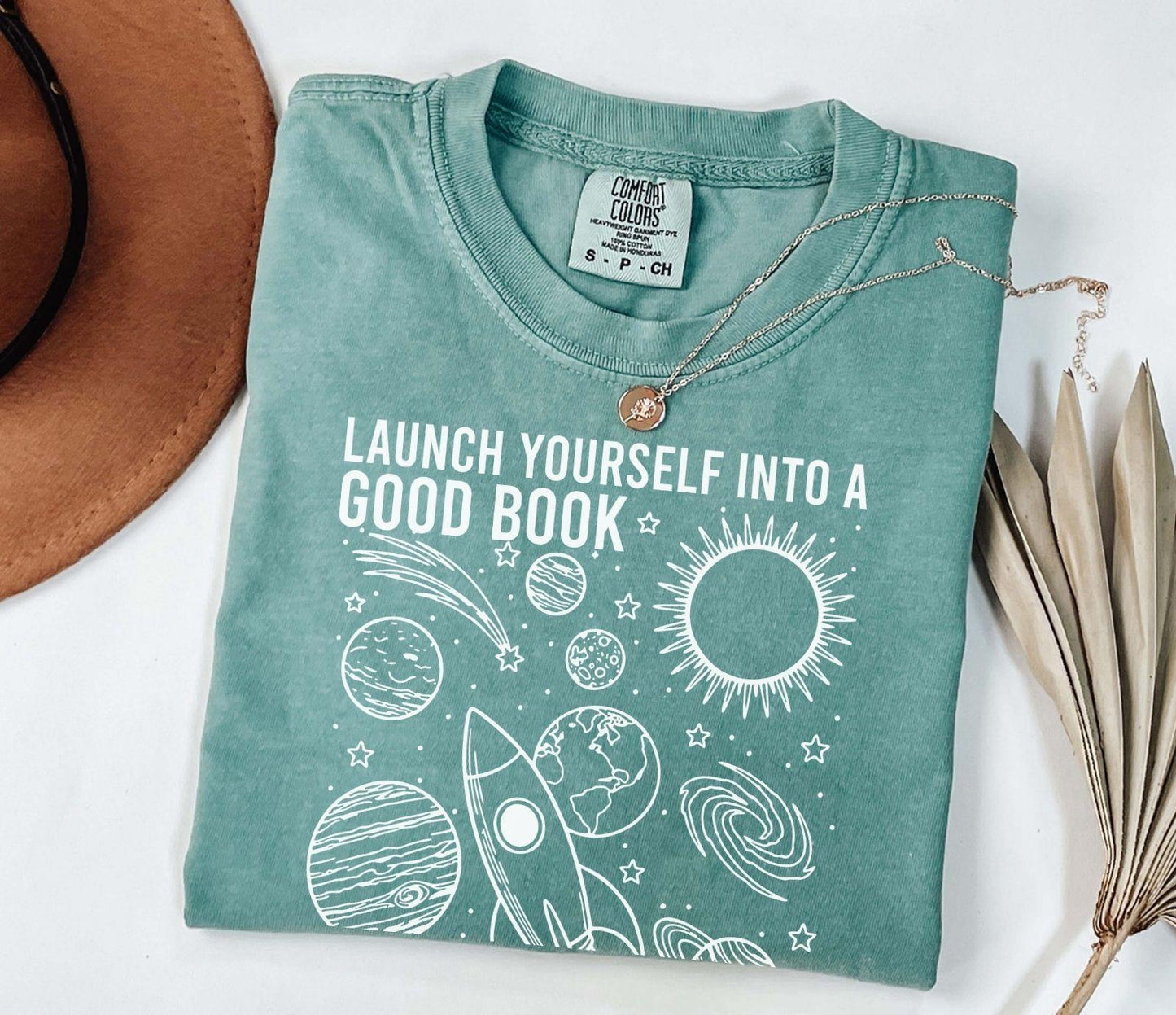 A comfort colors® shirt with the saying "launch yourself into a good book reading is out of this world"