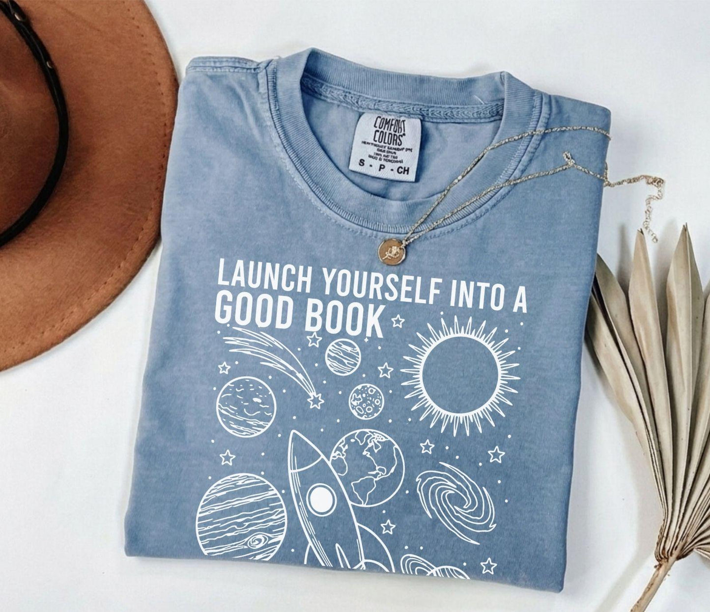 A comfort colors® shirt with the saying "launch yourself into a good book reading is out of this world"