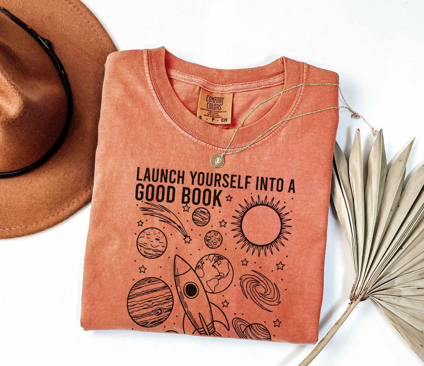 A comfort colors® shirt with the saying "launch yourself into a good book reading is out of this world"