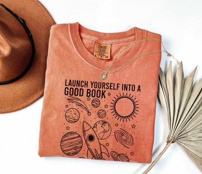 A comfort colors® shirt with the saying "launch yourself into a good book reading is out of this world"