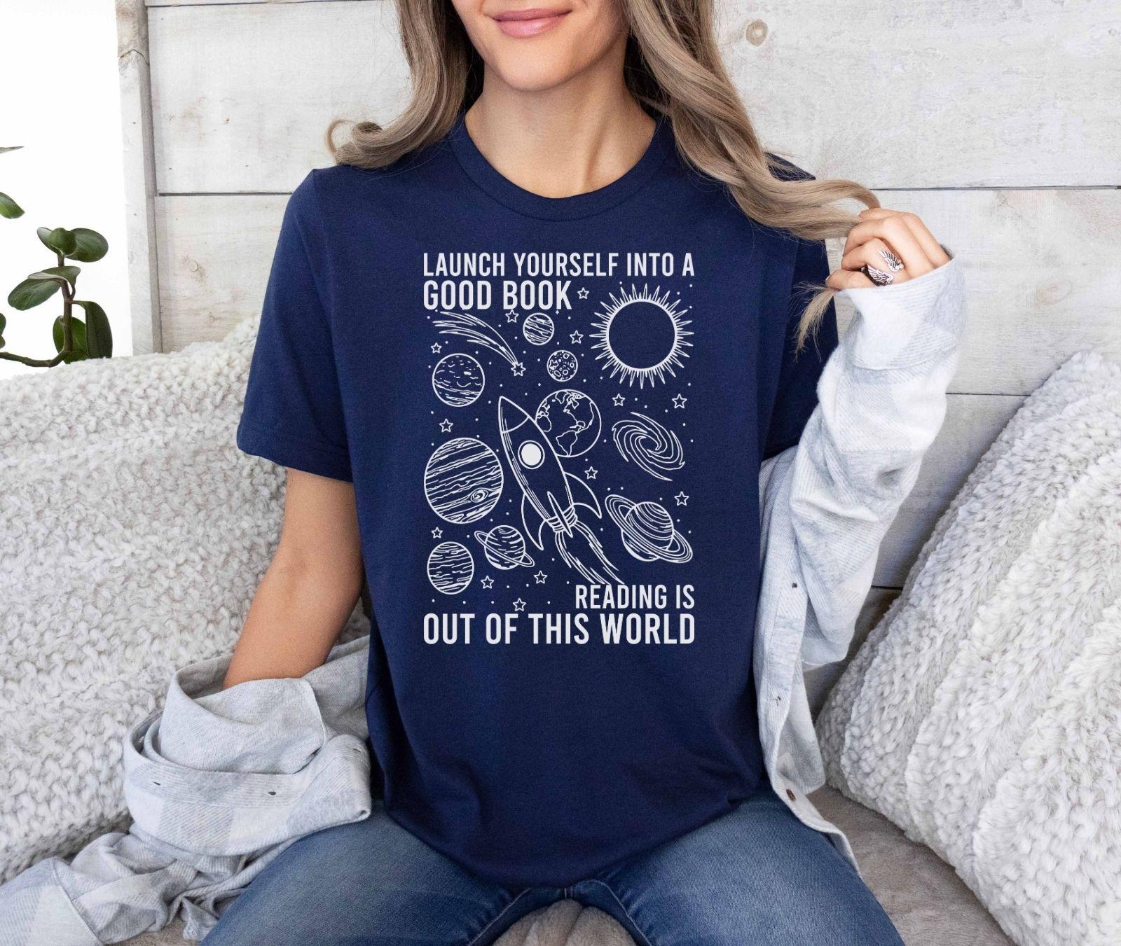 A bella canvas 3001 shirt with the saying "launch yourself into a good book reading is out of this world"