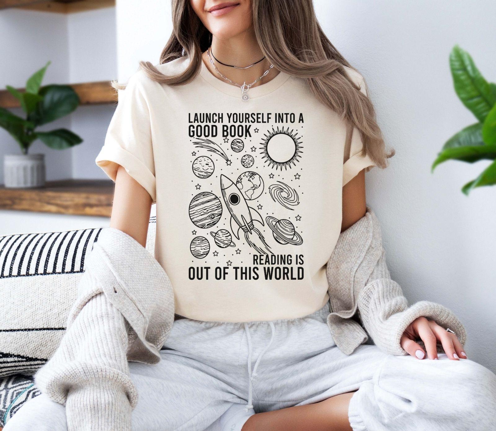 A bella canvas 3001 shirt with the saying "launch yourself into a good book reading is out of this world"