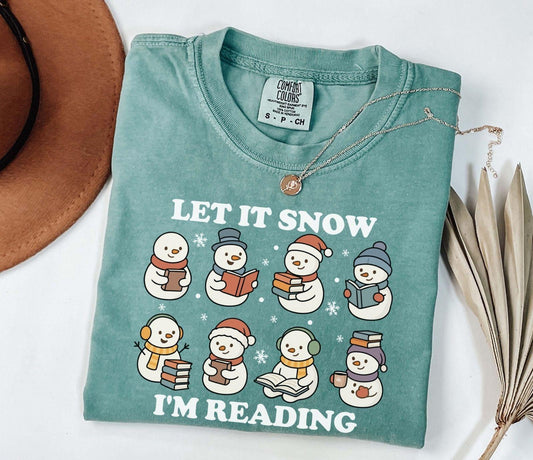 A comfort colors shirt with the saying "Let it snow I'm reading"