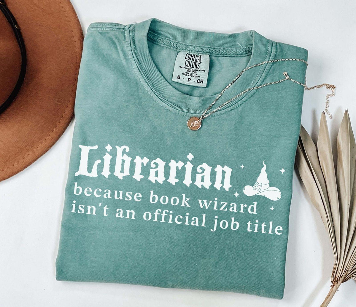 A comfort colors® shirt with the saying "librarian because book wizard isn't an official job title"