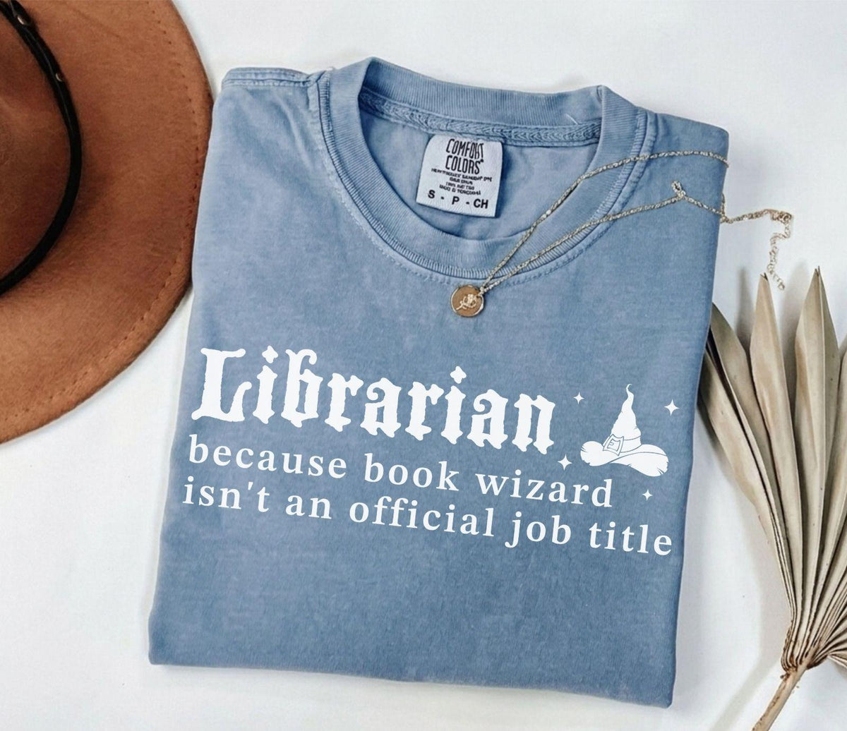 A comfort colors® shirt with the saying "librarian because book wizard isn't an official job title"