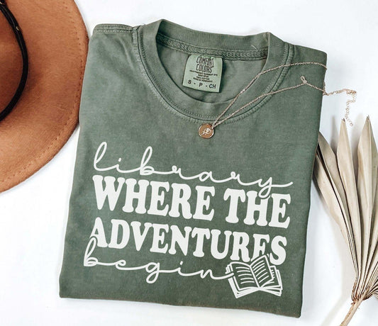 A comfort colors® shirt with the saying "library where the adventures begins"