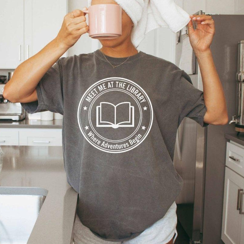 A comfort colors® shirt with the saying "meet me at the library where adventure begin"