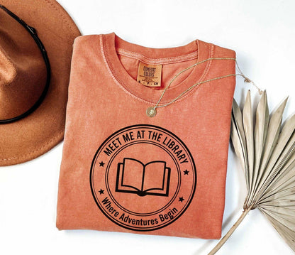 A comfort colors® shirt with the saying "meet me at the library where adventure begin"