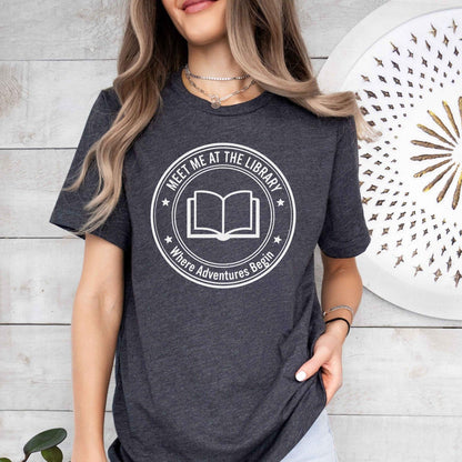 A comfort colors® shirt with the saying "meet me at the library where adventures begin"