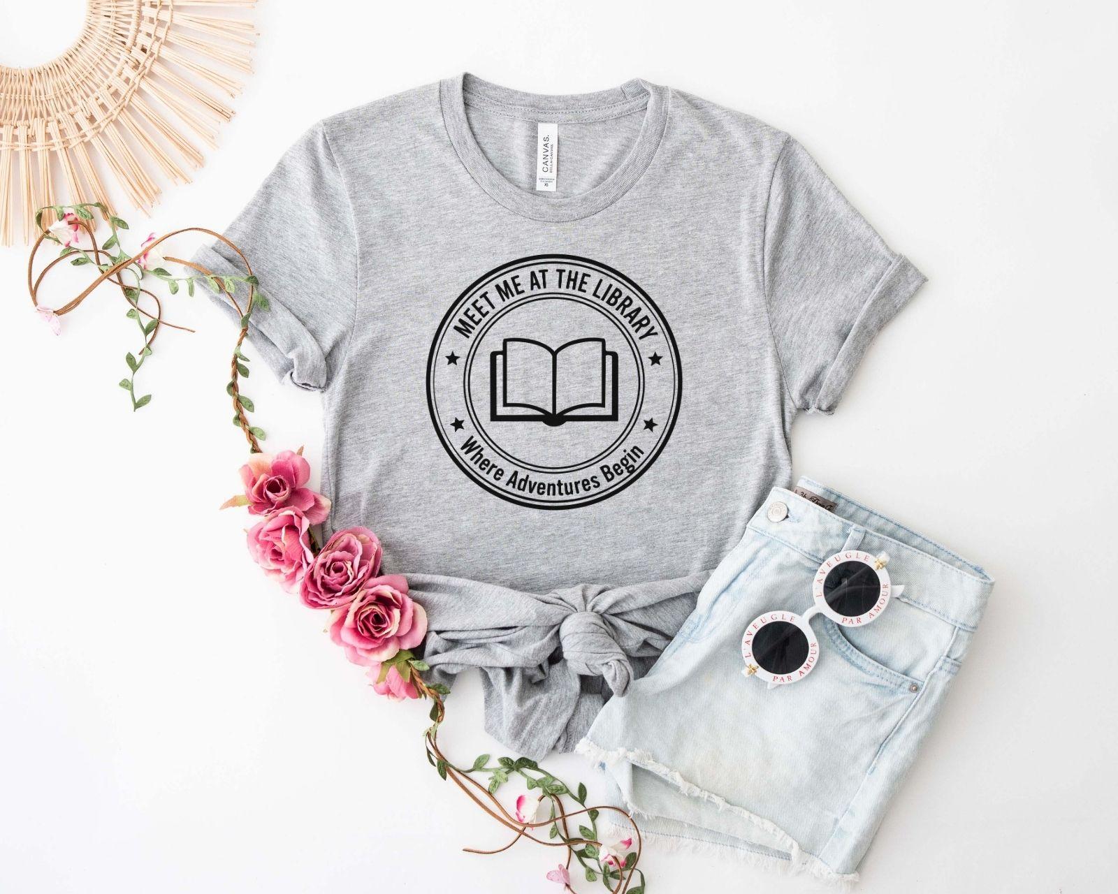 A comfort colors® shirt with the saying "meet me at the library where adventures begin"