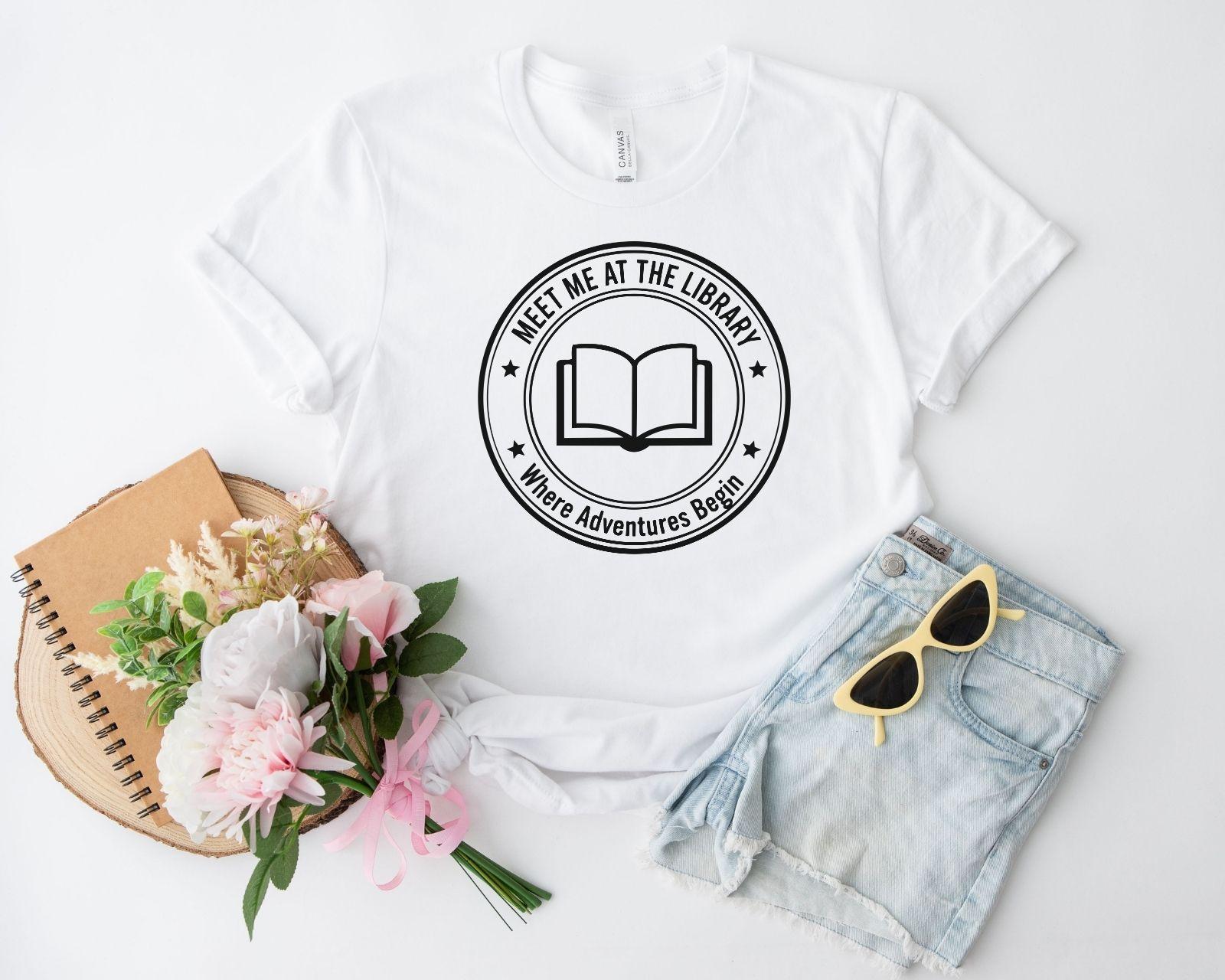 A comfort colors® shirt with the saying "meet me at the library where adventures begin"